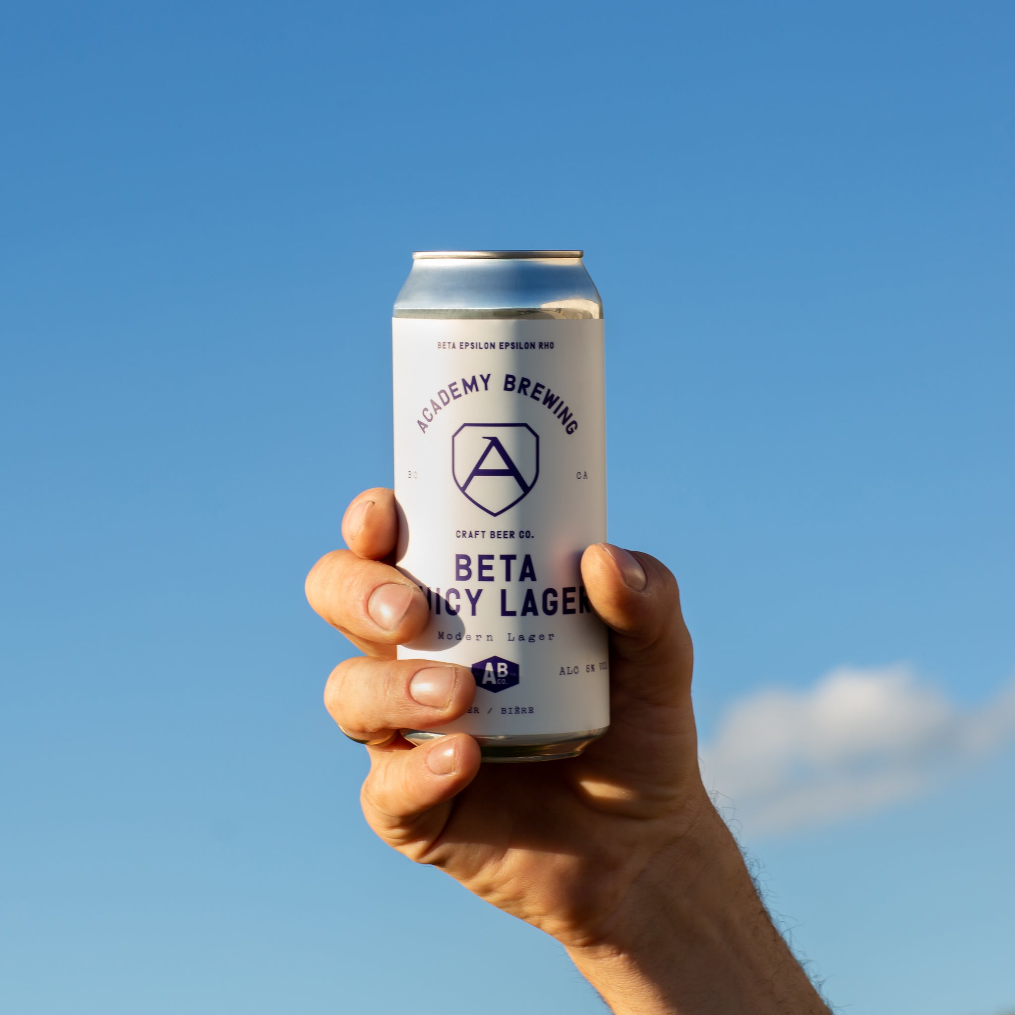 hand holding academy brewing beta juicy lager can up to the sky